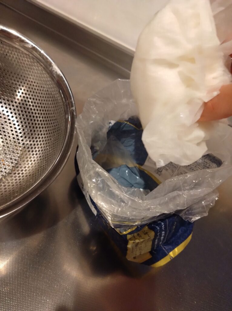 ヨーグルトを水切りしたキッチンペーパータオルを手で掴んでパンの空き袋に入れようとしている