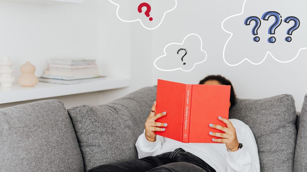 女性がソファーで本を読みながら疑問に思っている
