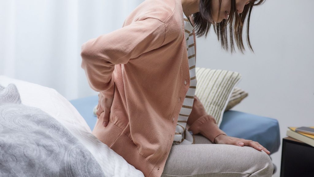 ベッドに腰掛け腰を押さえている女性